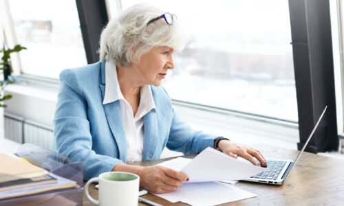 An older woman working at a desk with a laptop, analyzing Danish bookkeeping for Baltic Assist.